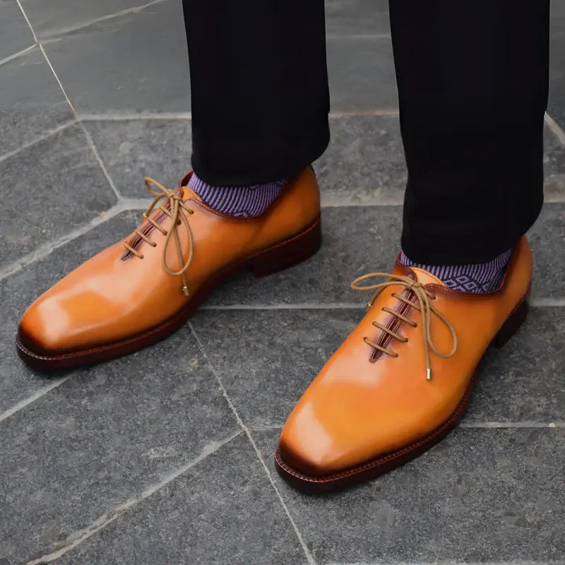 Man wearing golden wholecut oxford shoes, seamless leather construction